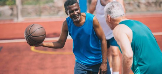 multiracial elderly men playing basketball together on playground on summer day